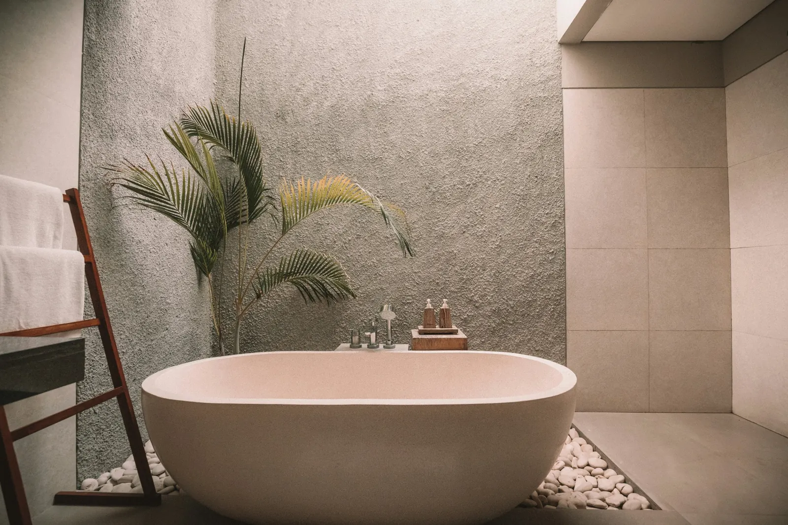 Bañera exenta de piedra junto a una palmera decorativa y piedras en un baño