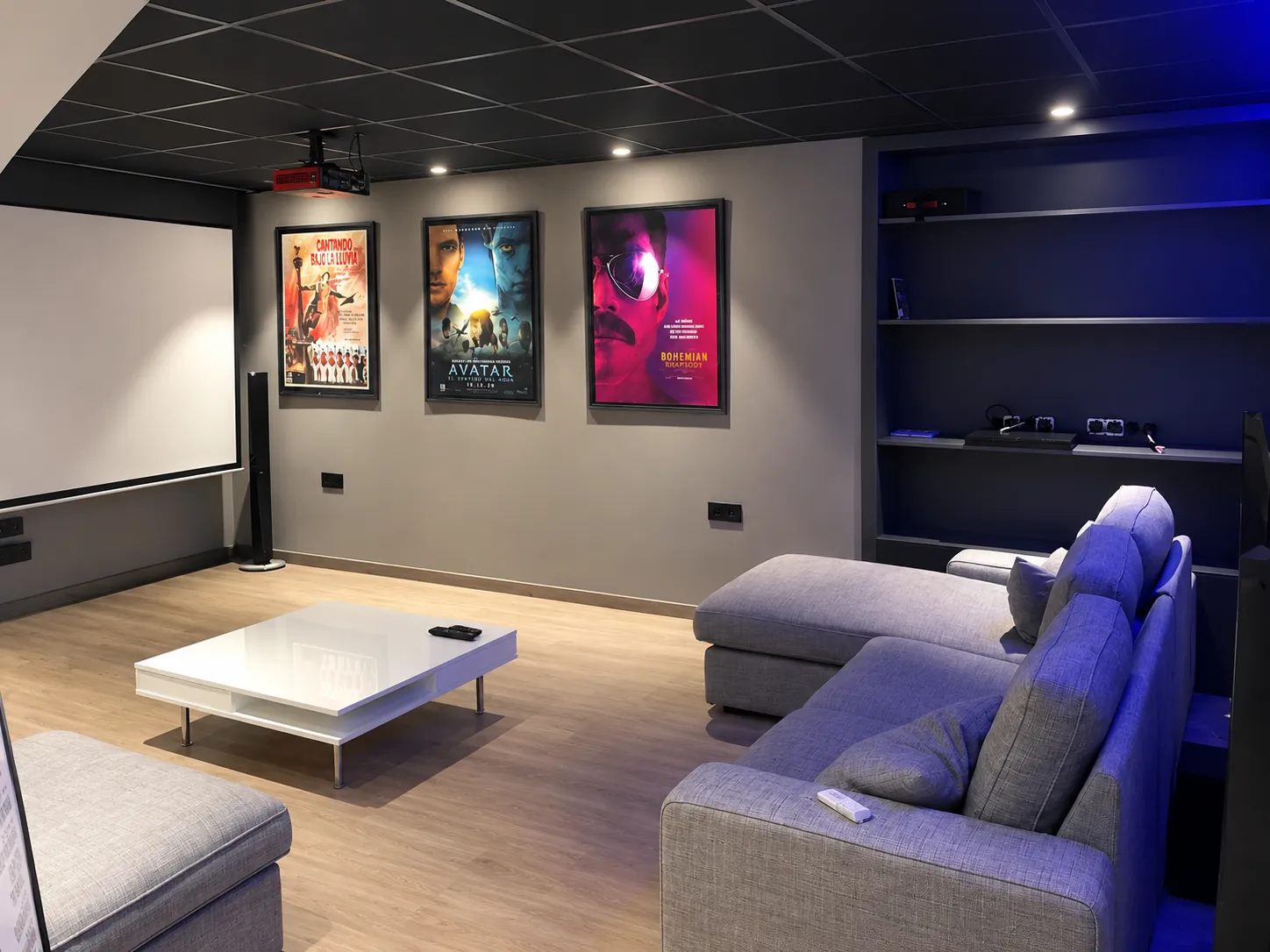 Sala de cine en casa con proyector, pantalla, sofá rinconero y estantería empotrada