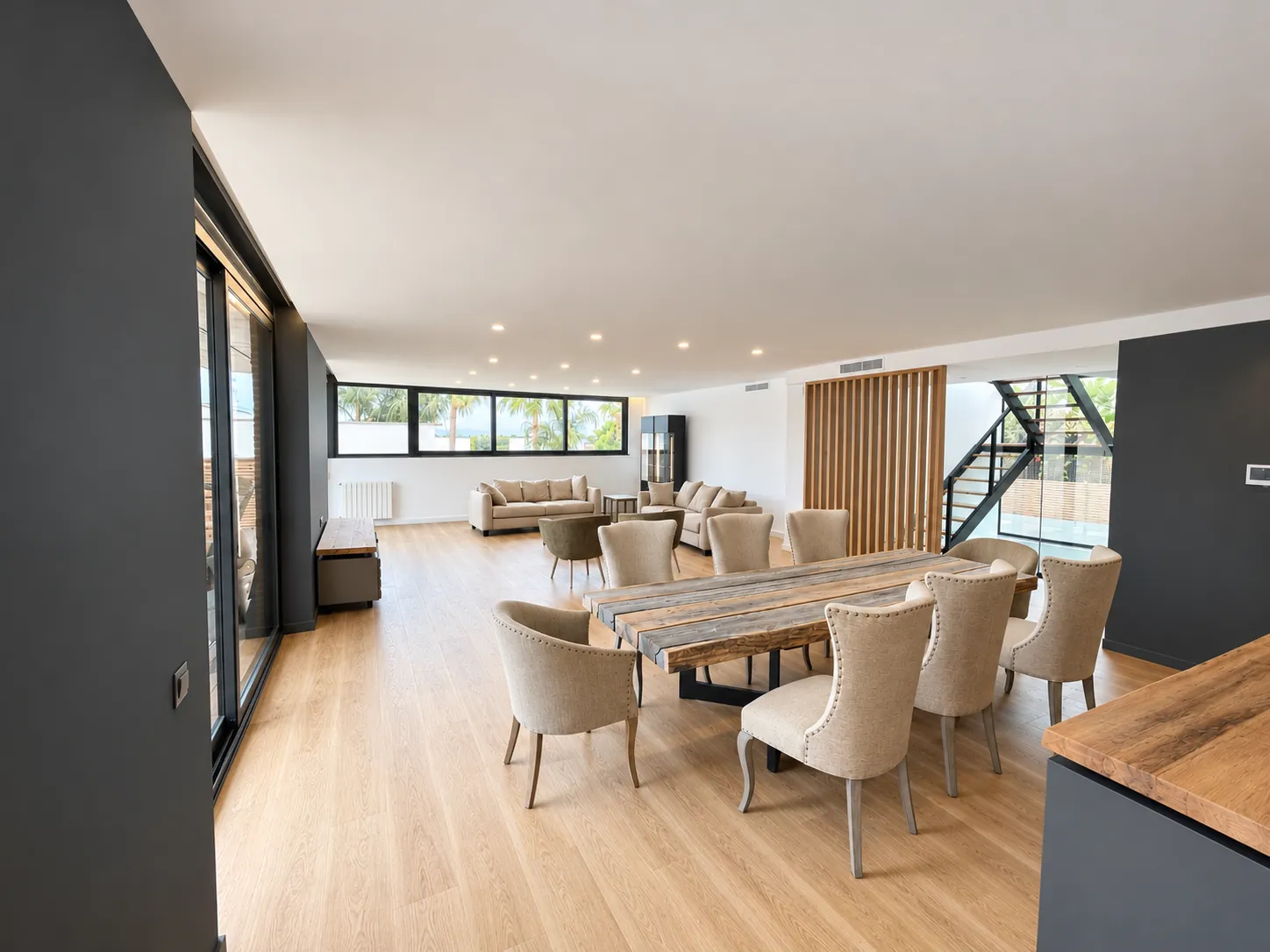 Salón comedor diáfano con suelo de madera, mesa de comedor y grandes ventanales