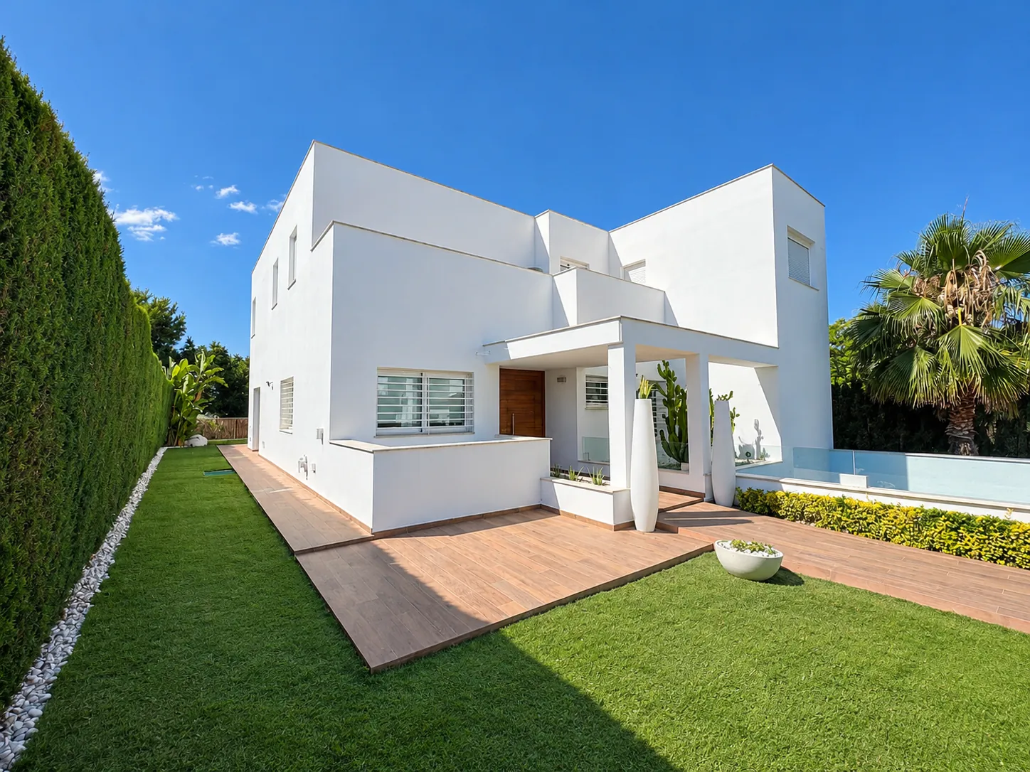 Fachada blanca de una vivienda con jardín de césped, pavimento cerámico y piscina